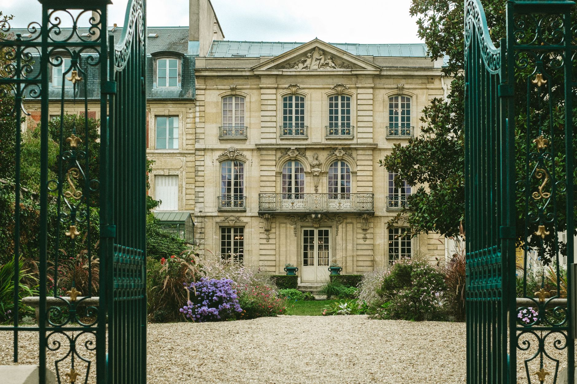 Open wrought iron gates in front of a stone house and garden